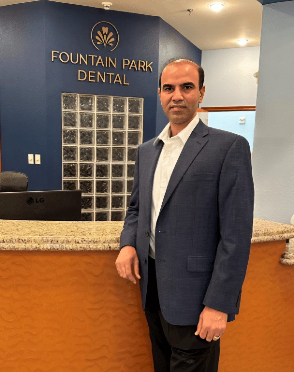 Dentist Flower Mound TX Girish Chaudhari Standing At Front Desk HP Dr. Girish Chaudhari is seen in a nice suit standing in front of the reception desk at Fountain Park Dental